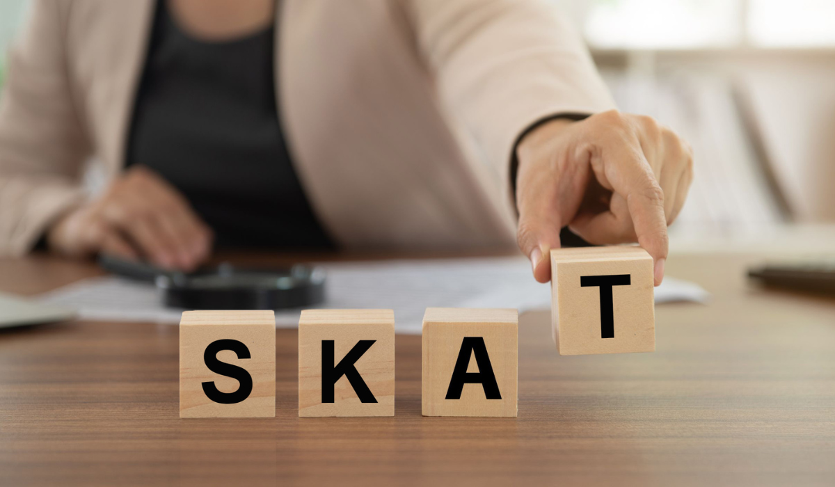 Billedet viser en person, som stiller fire klodser ved siden af hinanden. På hver klods er der et bogstav, som tilsammen giver ordet 'SKAT'